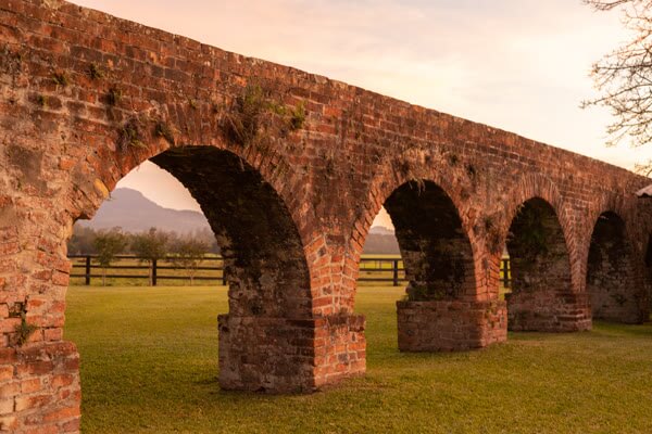 Aqueduto histórico de tijolos vermelhos em campo verde no entardecer