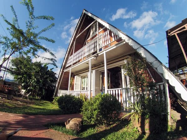 Exterior de cabana de madeira em formato de A com corrimãos brancos e jardim