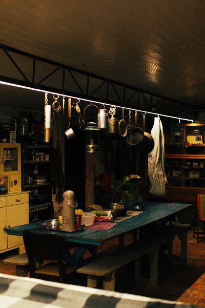 Sala de jantar compartilhada com mesa azul e panelas penduradas na cozinha