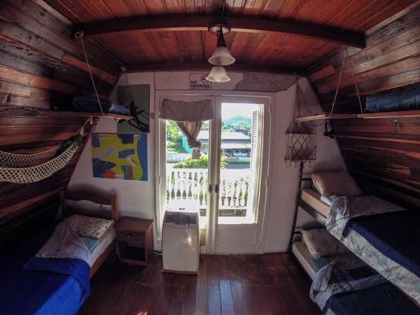 Quarto de dormitório rústico em madeira com beliches, rede e portas para a varanda