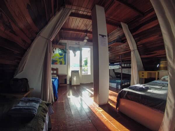 Dormitório compartilhado com cortinas de tecido, camas de madeira e varanda ensolarada