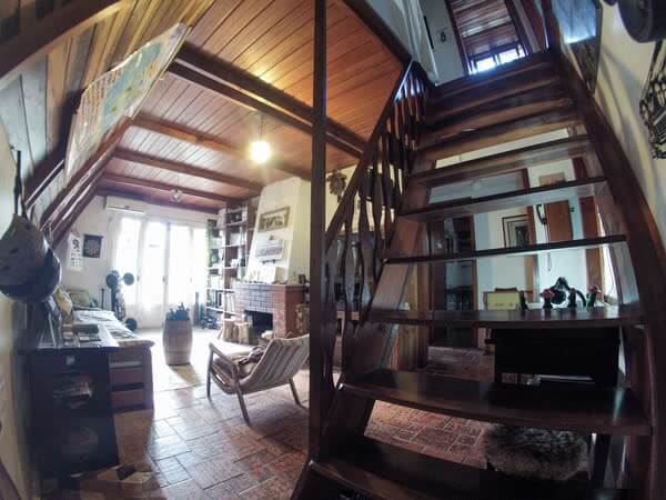 Sala de estar com escada de madeira, lareira de tijolos e mapa-múndi