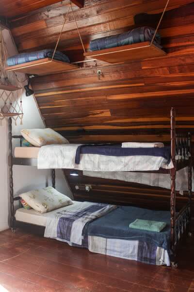 Beliche de madeira com prateleiras suspensas por cordas em quarto estilo cabana